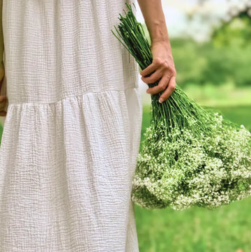 Person wearing a white dress holding a bouquet of flowers in a natural setting